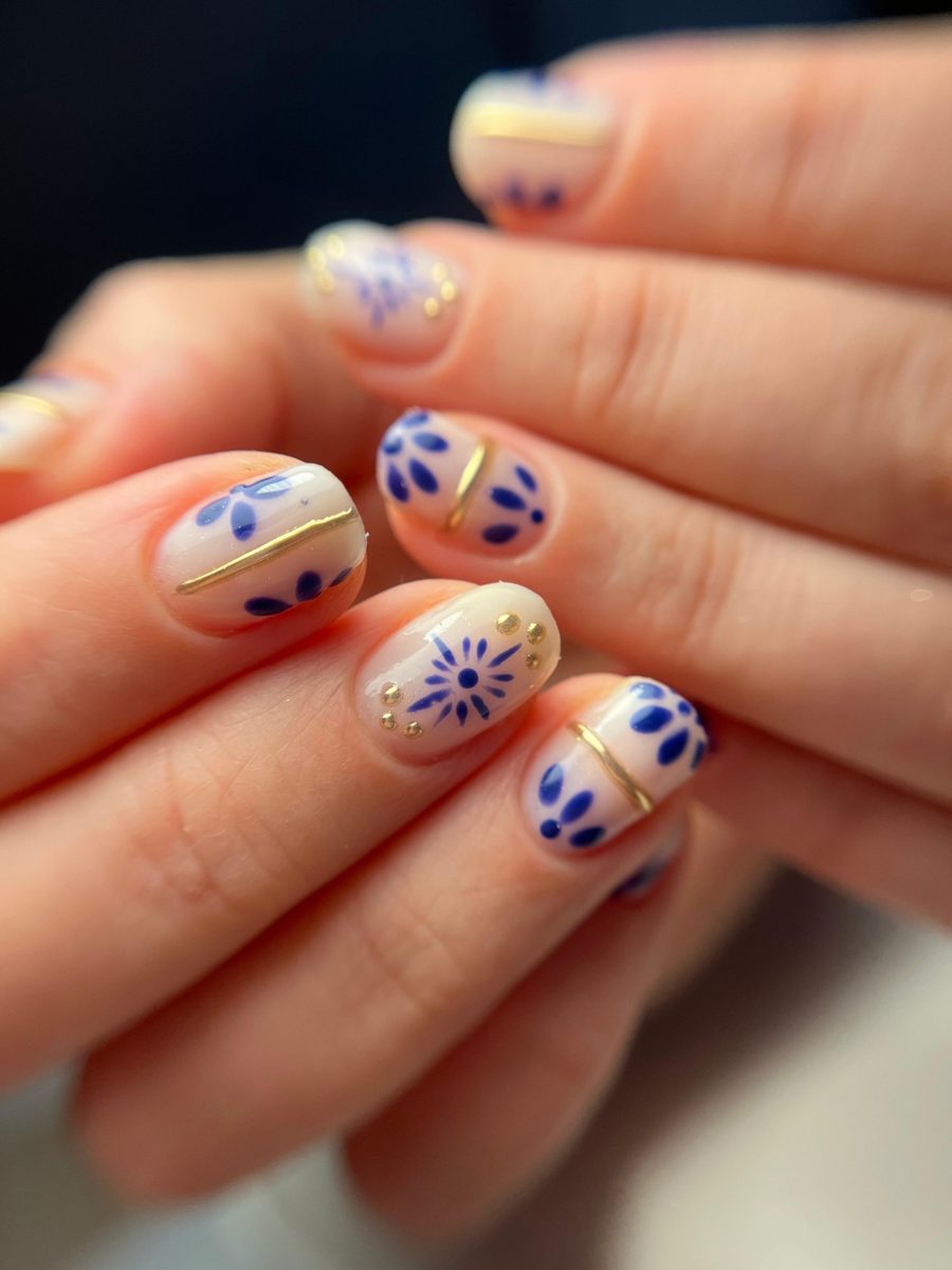 Nail art met blauwe bloemetjes en gouden accenten op korte nagels